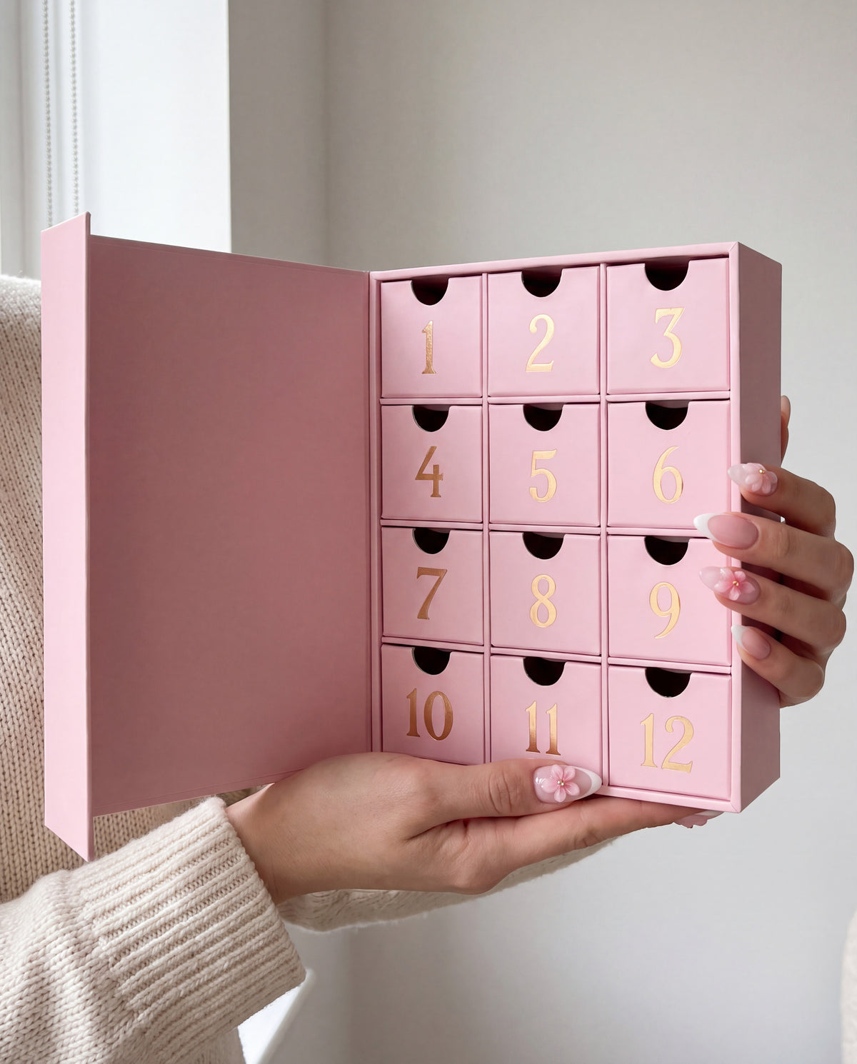 12 cases — Une main tient le petit calendrier de l'Avent ouvert, avec ses 12 tiroirs.