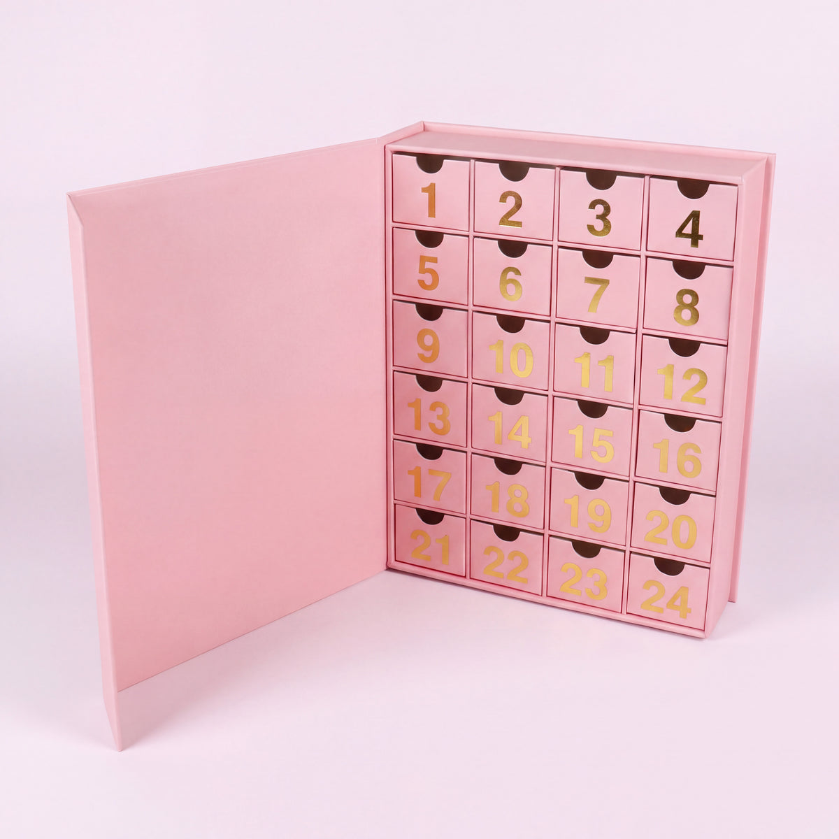 24 cases — Calendrier de l'Avent bijoux ouvert vu de face, tiroirs numérotés dorés sur fond rose pâle.